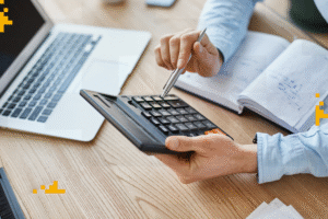 Pessoa usando calculadora para calcular juros abusivos em uma dívida, com livros e laptop ao fundo, destacando a importância de entender encargos financeiros ilegais.